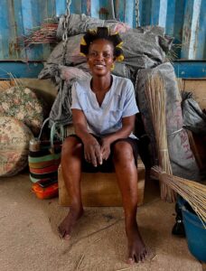 Babatree Baskets (Ghana) artisan smiling at the camera, surrounded by baskets.